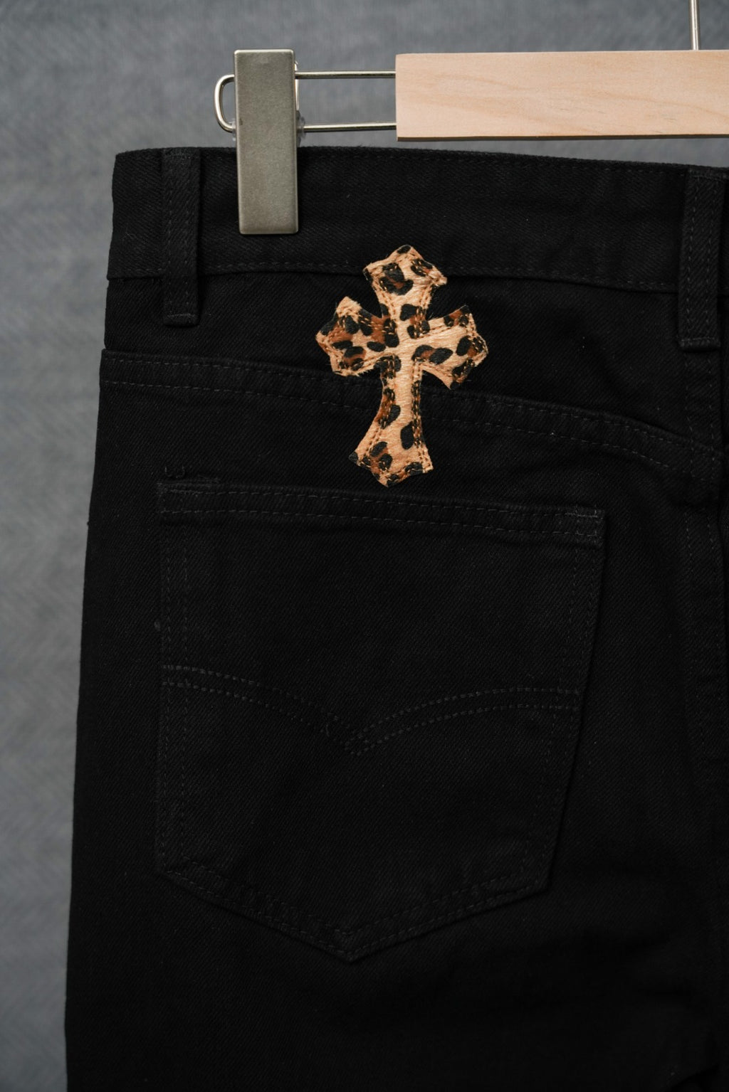Black pants with central purple-gold cross patch, front pocket and waistband detail.