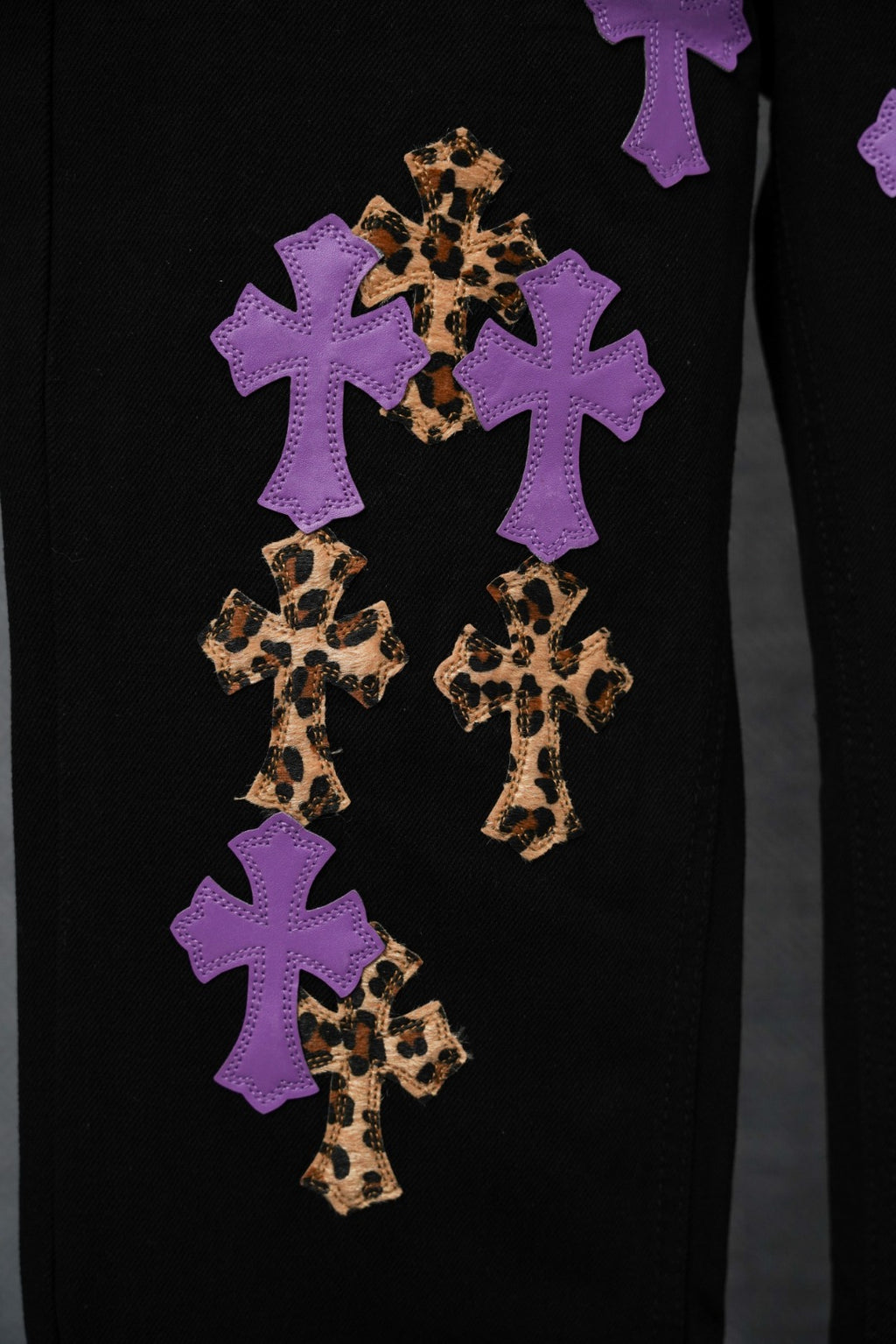Black pants close-up: purple and gold cross patches with leopard-pattern accents.