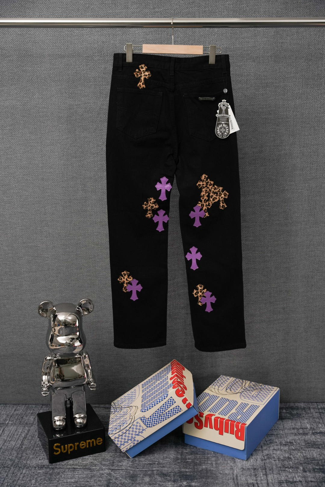 Black pants with purple and gold cross patches and small hanging tag, straight leg.