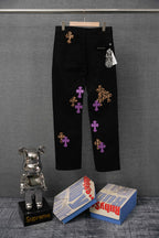 Black pants with scattered purple and gold cross patches, side view on hanger.