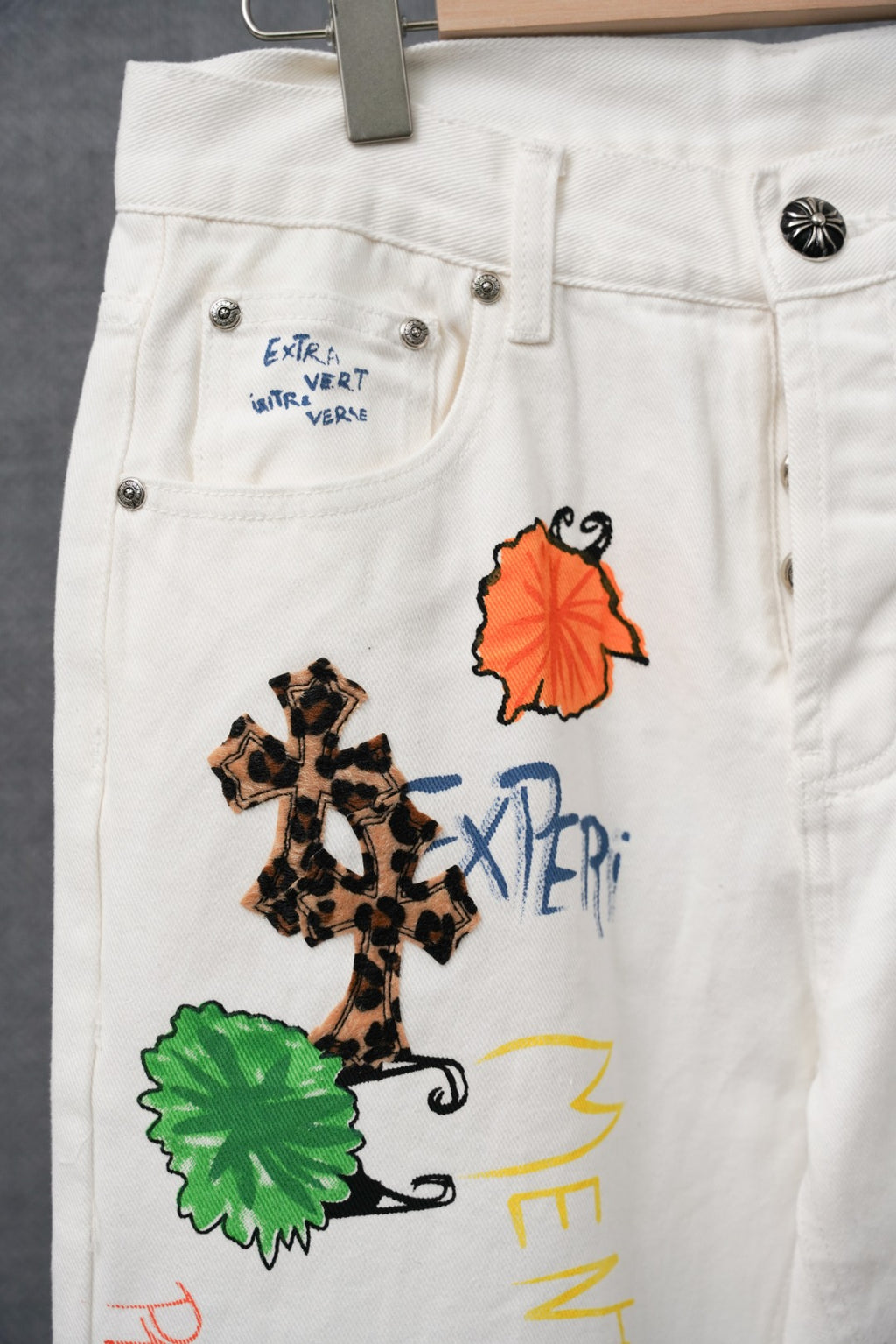 White denim pants close-up with stitched green and orange patches and crossed design