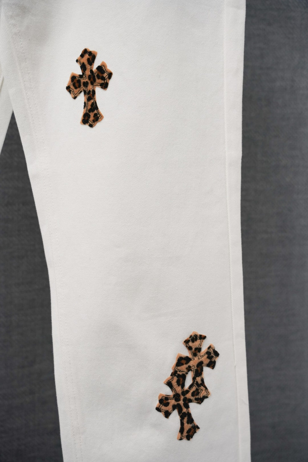 White graphic pants close-up showing two leopard-print cross patches on the leg