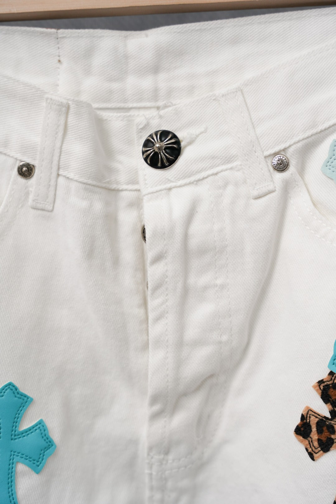 White denim pants with blue cross patch detail and metal button at waistband