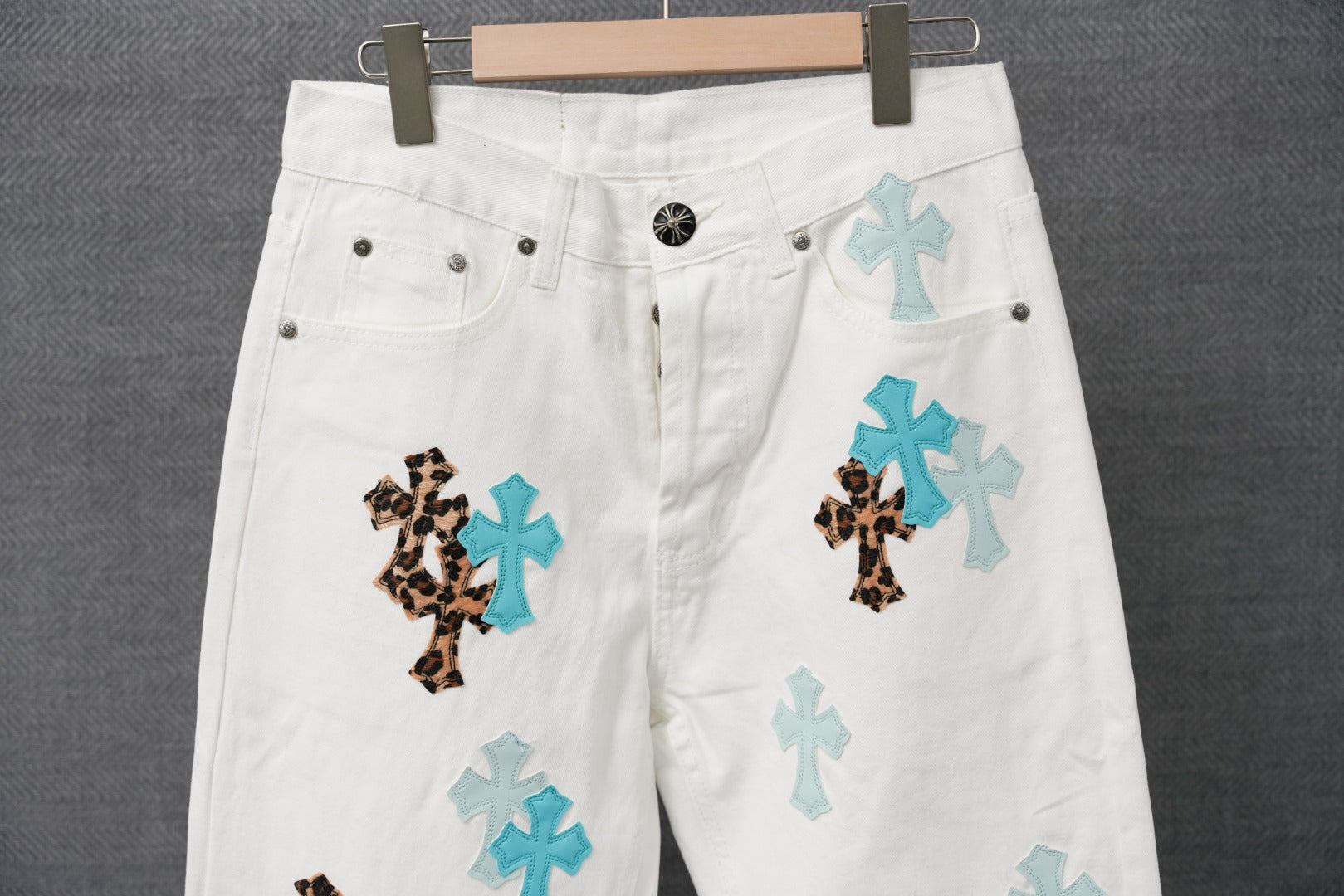 White denim pants with blue and leopard cross patches, front close-up