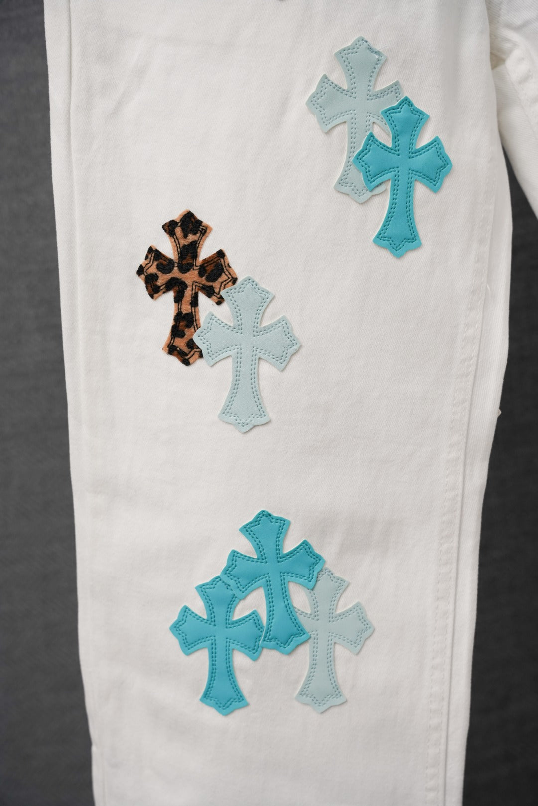 White denim pants with blue cross patch appliques along the leg