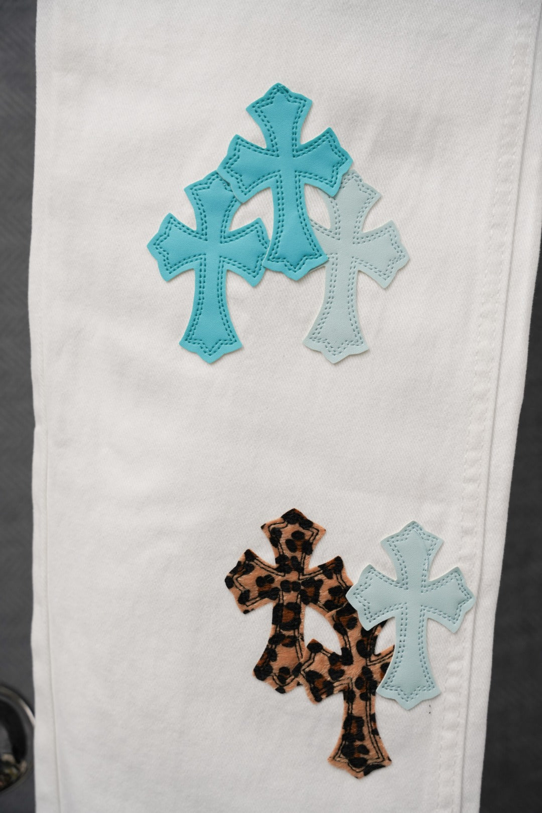 White denim pants with stacked blue cross and leopard cross patches on the leg