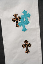 White denim pants with blue and leopard cross patches, mid-leg view