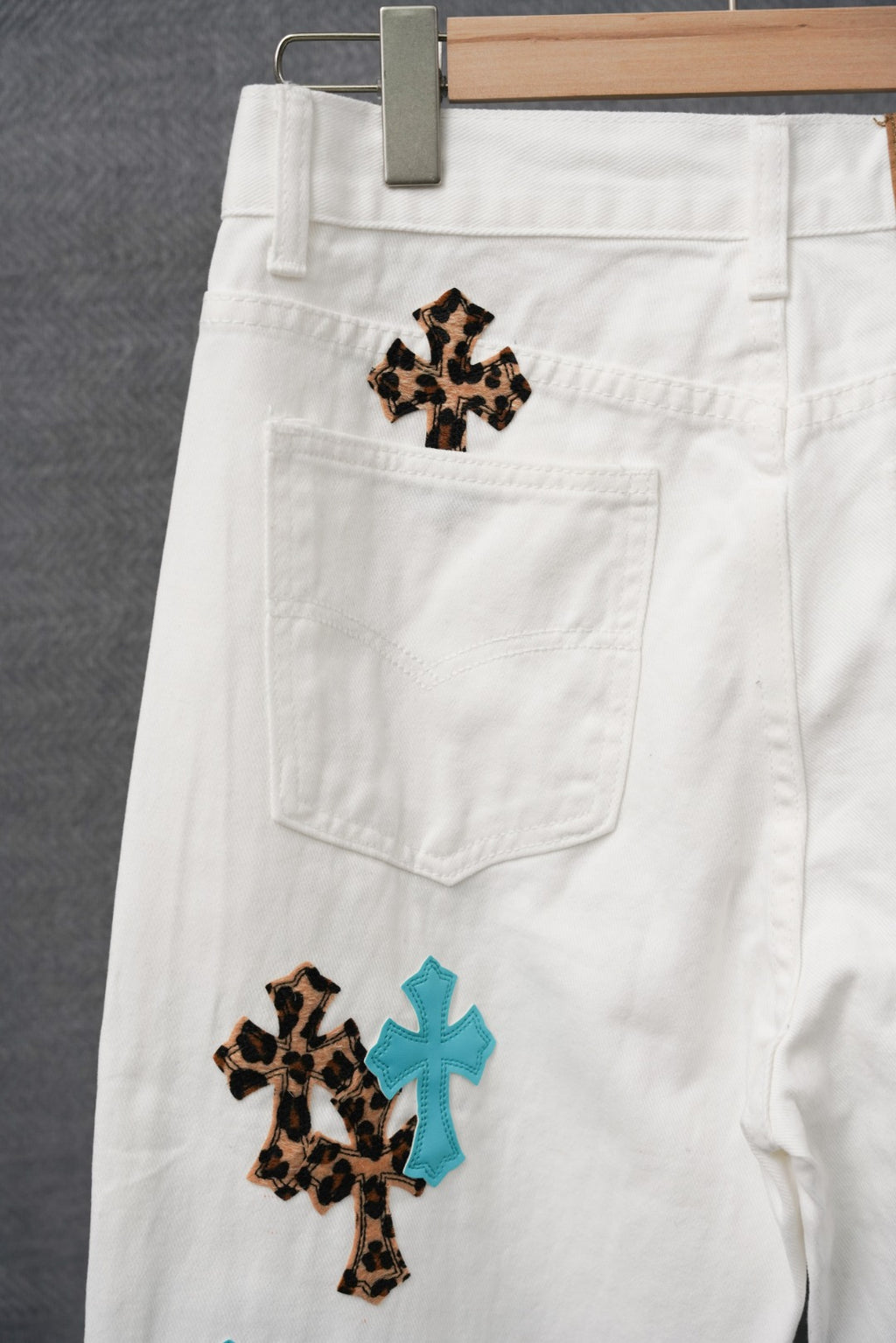 White pants with leopard and teal cross patches near the front pocket