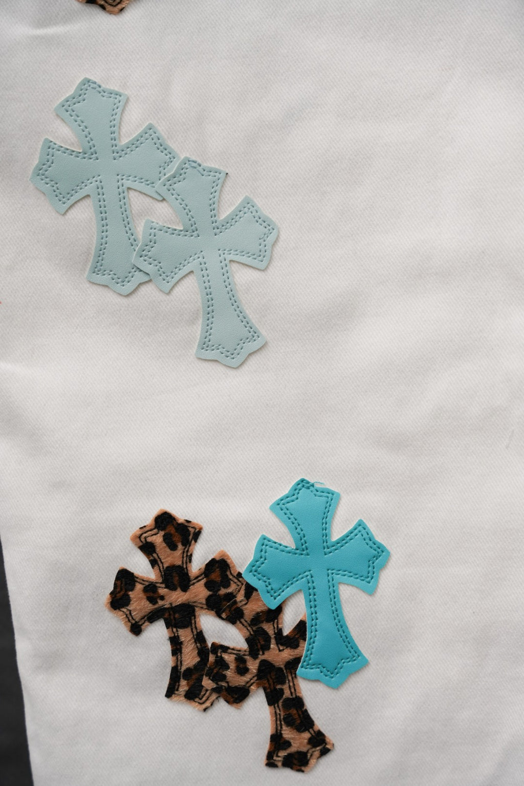 White pants with teal cross appliqué patches and a leopard cross patch
