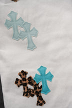 White pants with teal cross appliqué patches and a leopard cross patch