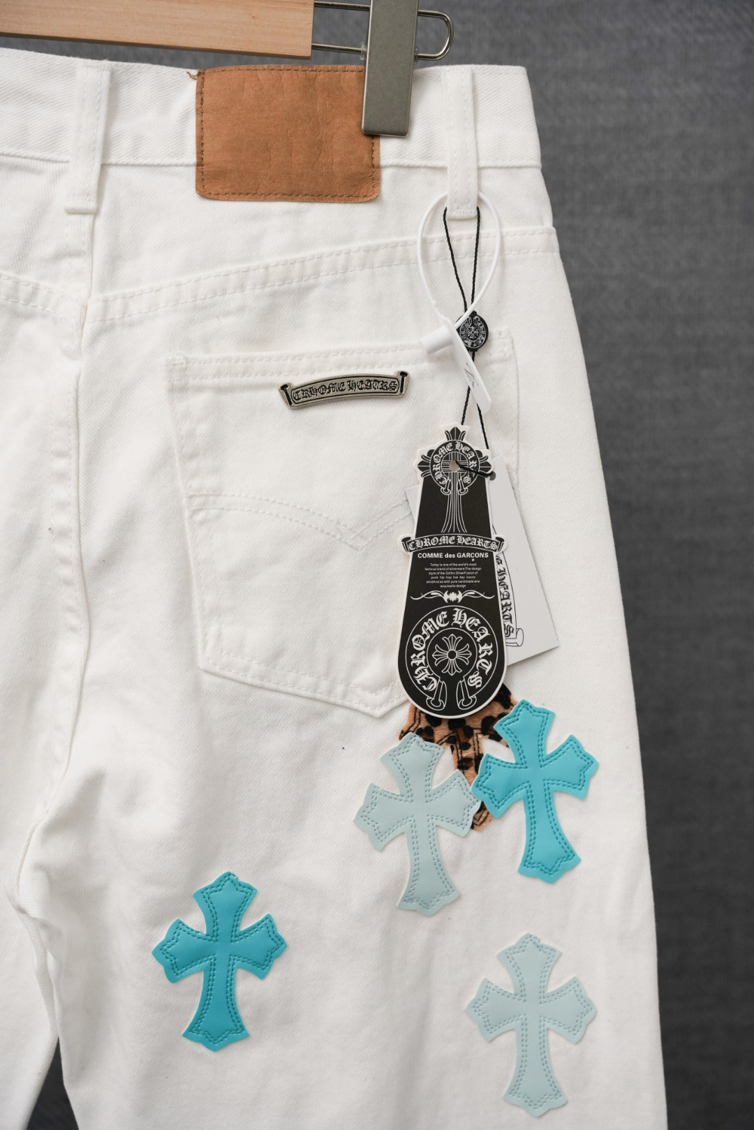 White pants with teal and leopard cross patches and hanging logo tag