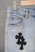 Light-wash denim pants front with button closure and a black cross patch