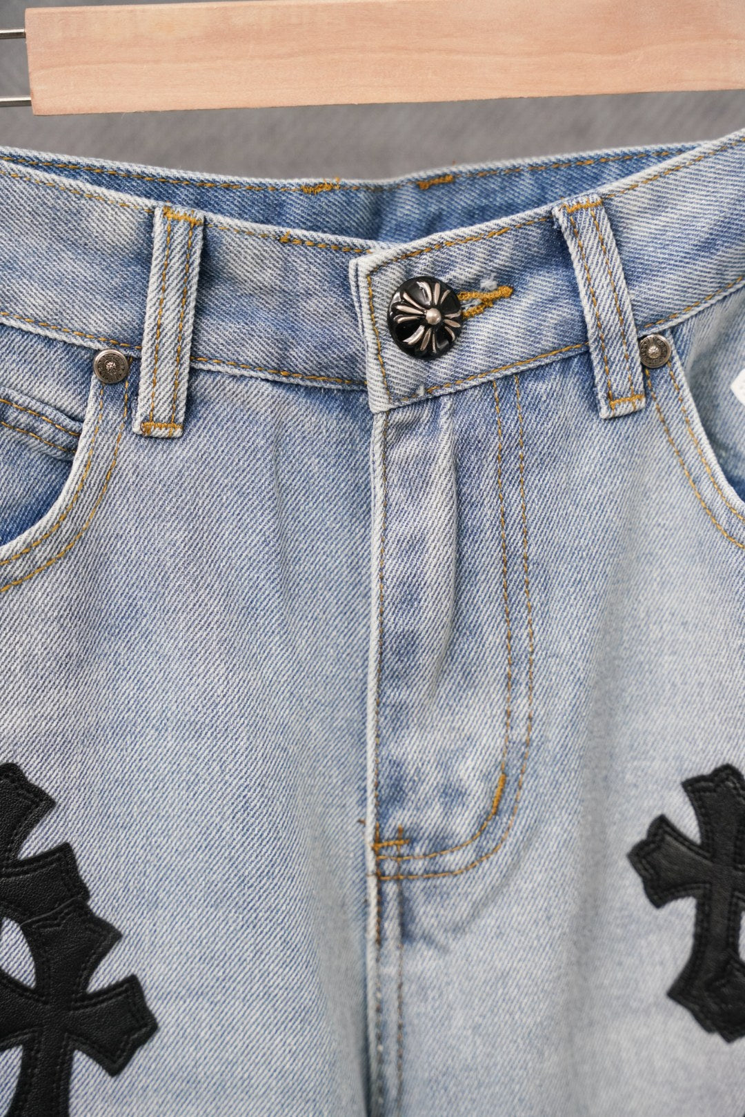 Light-wash denim pants close-up of belt loops and embroidered cross patches