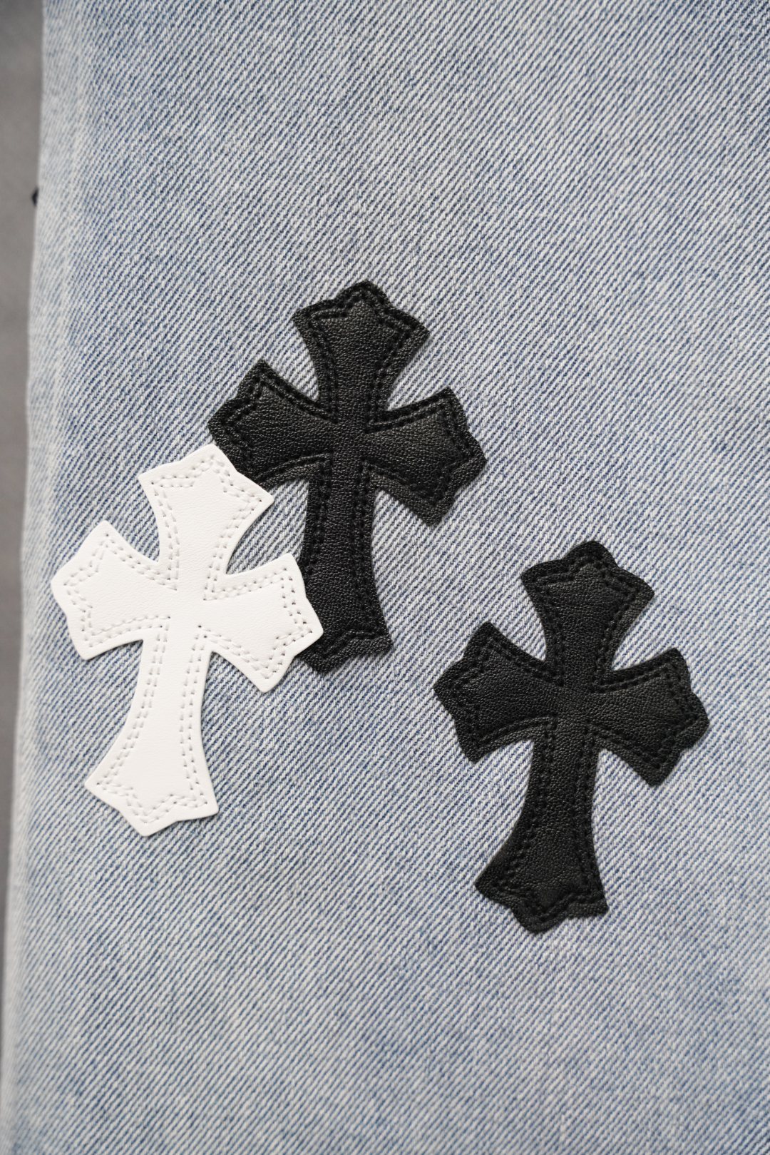 Close-up of light blue denim leg with black and white cross appliques