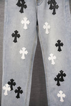 Light-wash denim pants with repeating black and white cross patches across the front