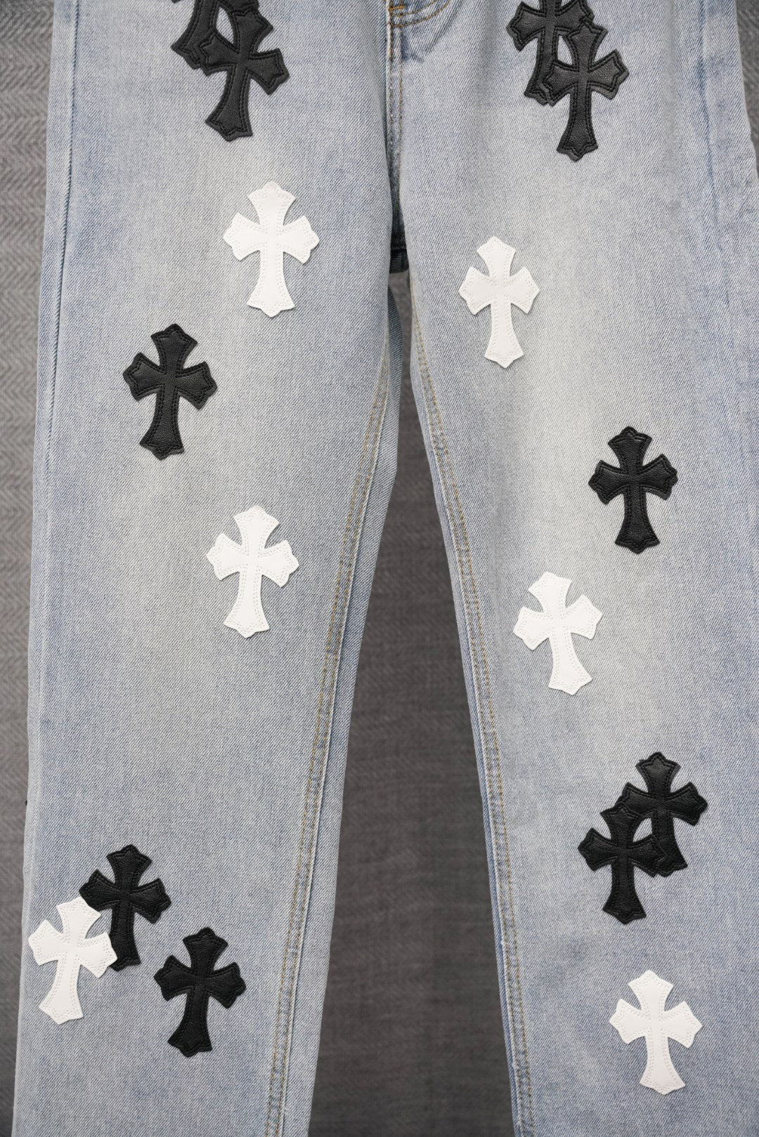 Light-wash denim pants with repeating black and white cross patches across the front