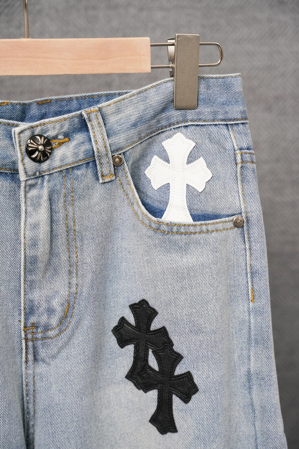 Light blue denim jeans with button fly, black and white cross patches