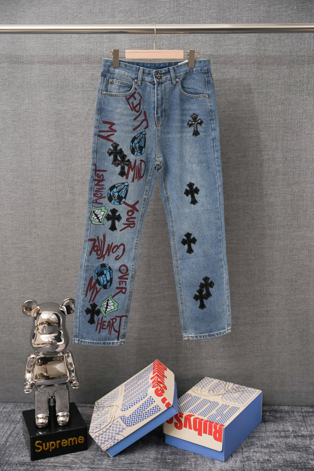 Light blue denim pants with colorful graffiti print and black cross patches on legs