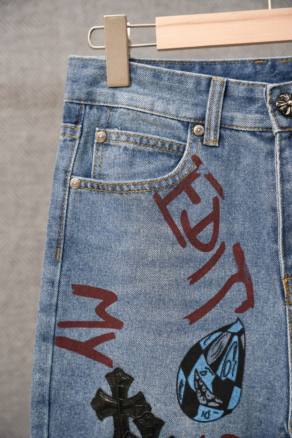 Light blue denim pants with large red graphic print and black cross patch on front.