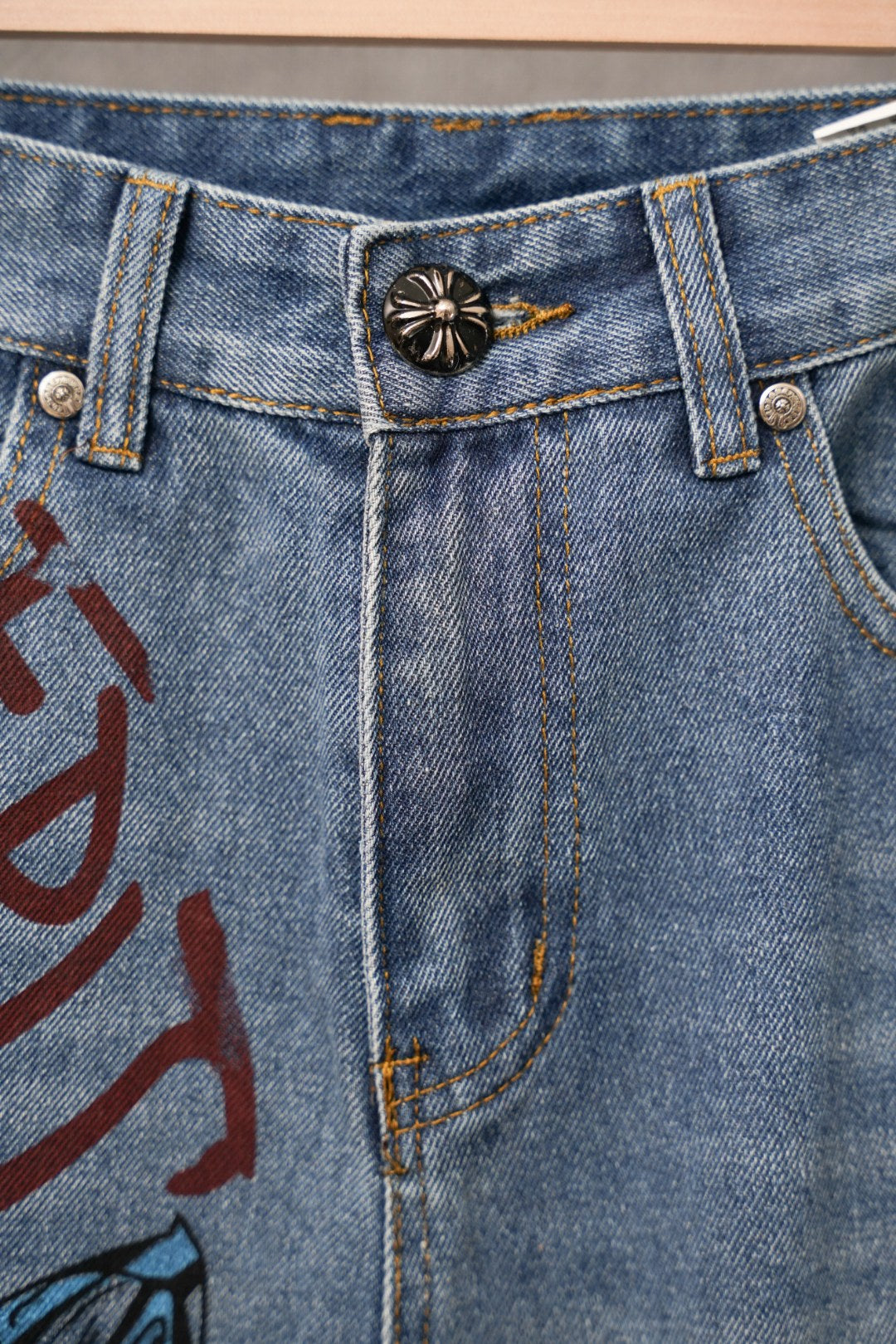 Light blue denim jeans front with button fly and black sun-shaped patch on waistband.