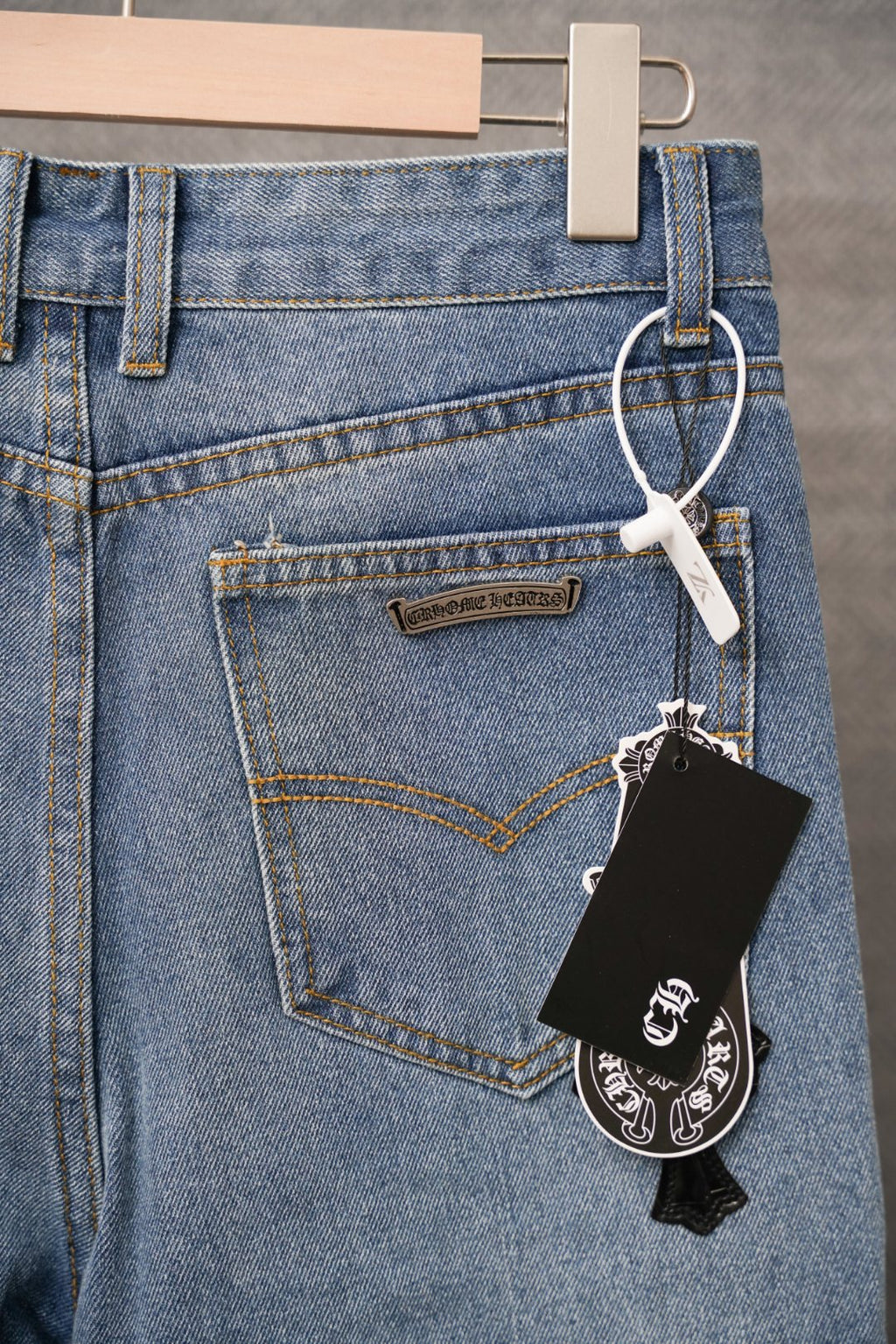 Light blue denim pants with rear patch tag and black cross charm on belt loop.