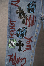 Light blue denim pants with colorful face and text graphic print and cross patches.