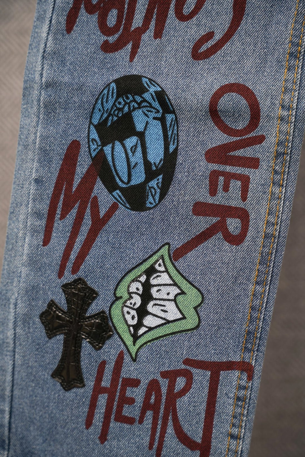 Light blue denim pants with face graphic and red text-style print near pocket.