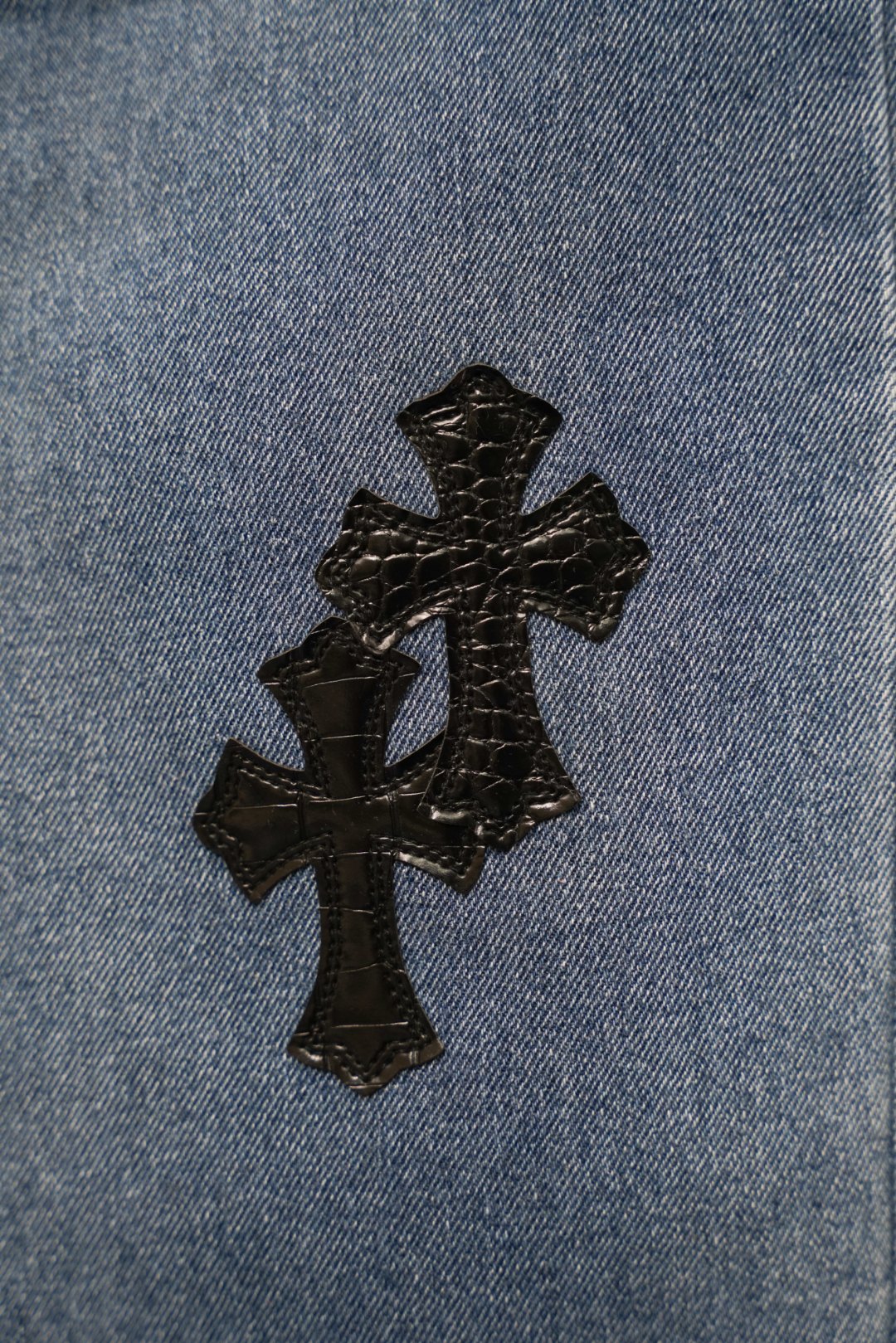 Light blue denim fabric with three stitched black cross patches.