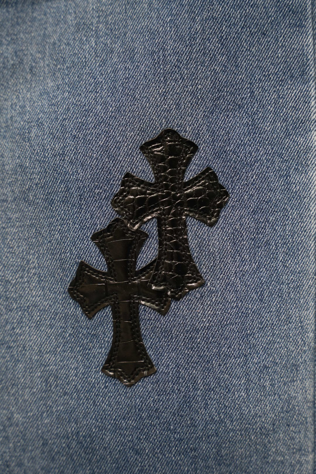 Light blue denim close-up with stitched black cross patch applique