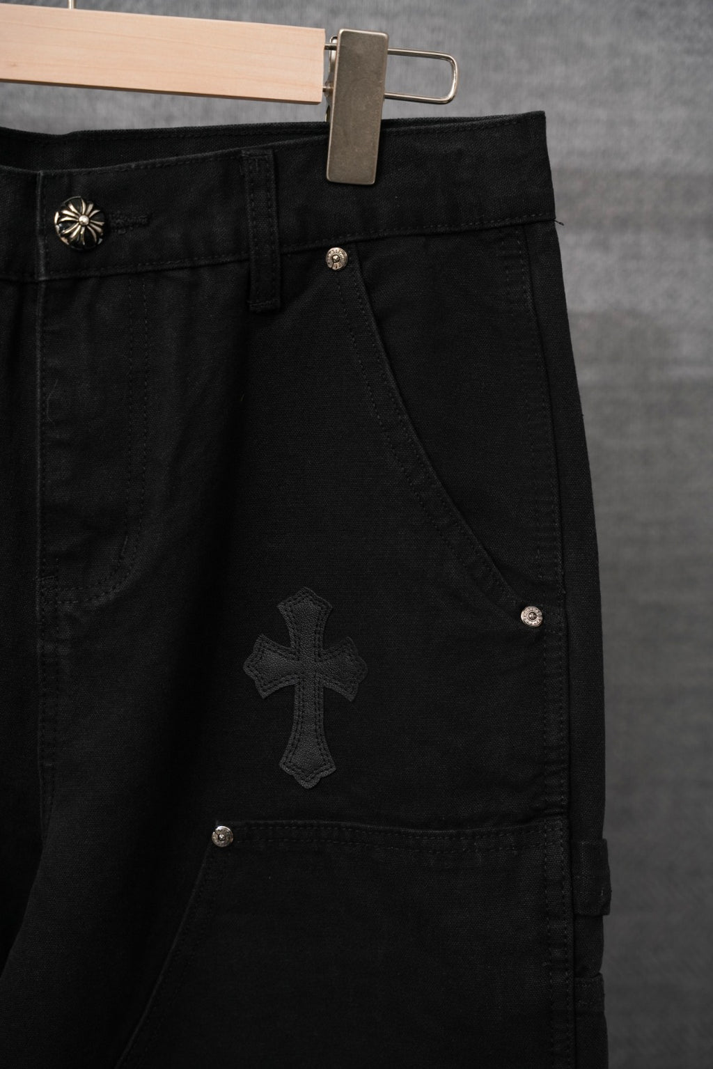 Black cargo pants with large cross patch and metal snap button