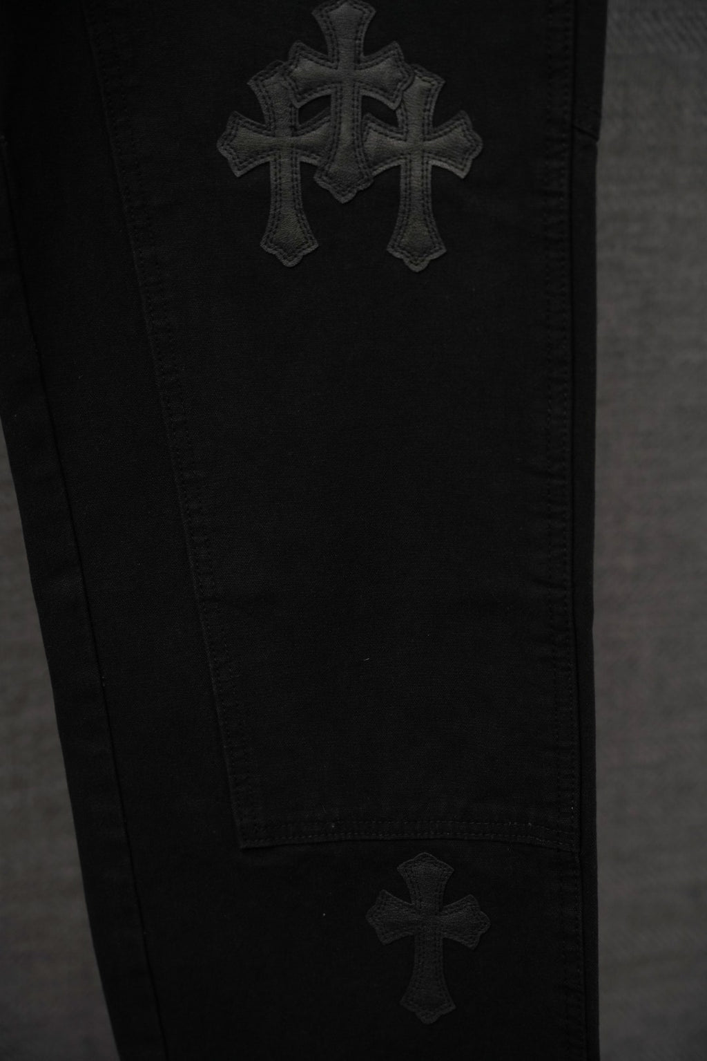 Black chrome pants close-up with stacked cross embroidery on leg