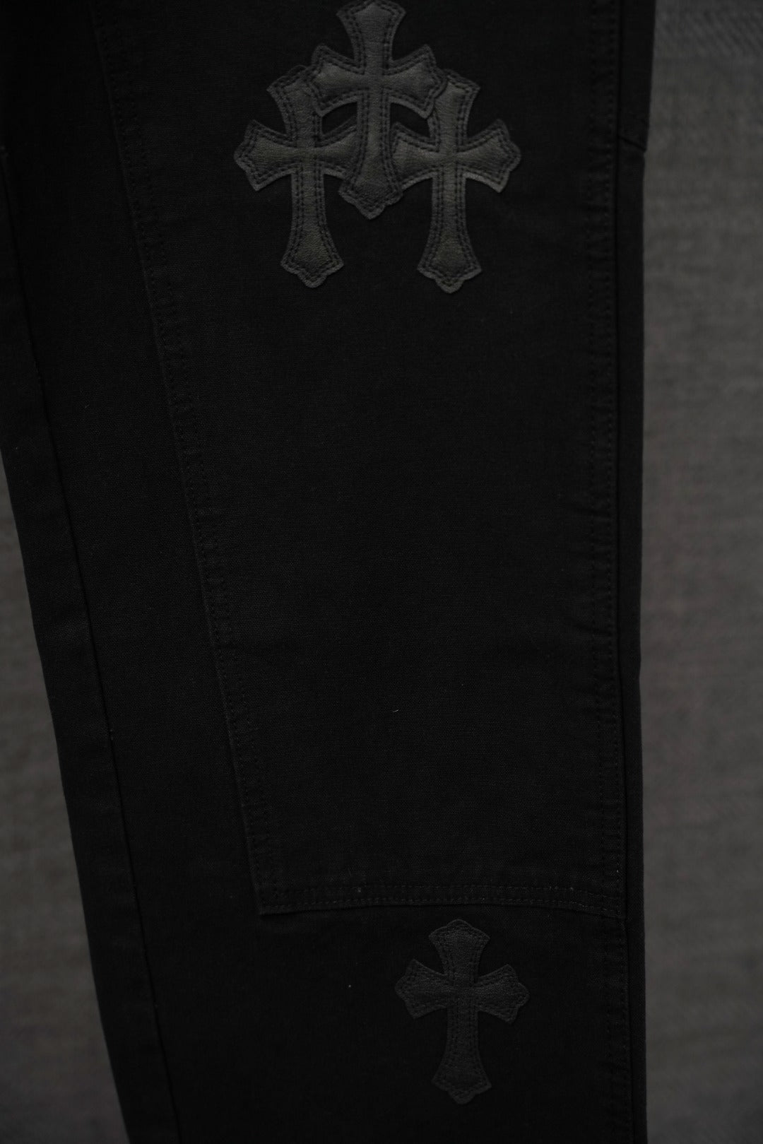 Black chrome pants close-up with stacked cross embroidery on leg