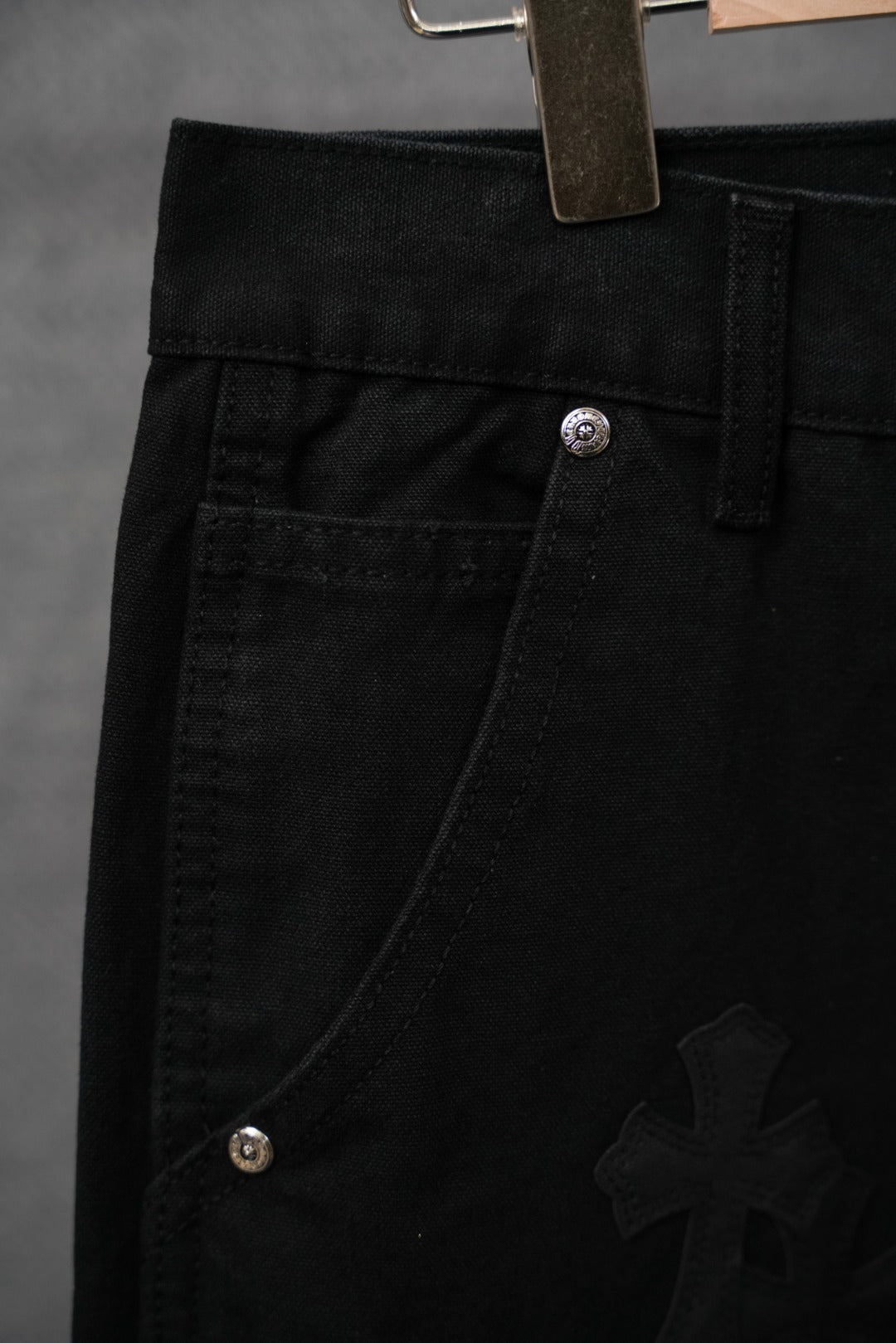 Black chrome pants close-up with diagonal pocket seam and cross embroidery