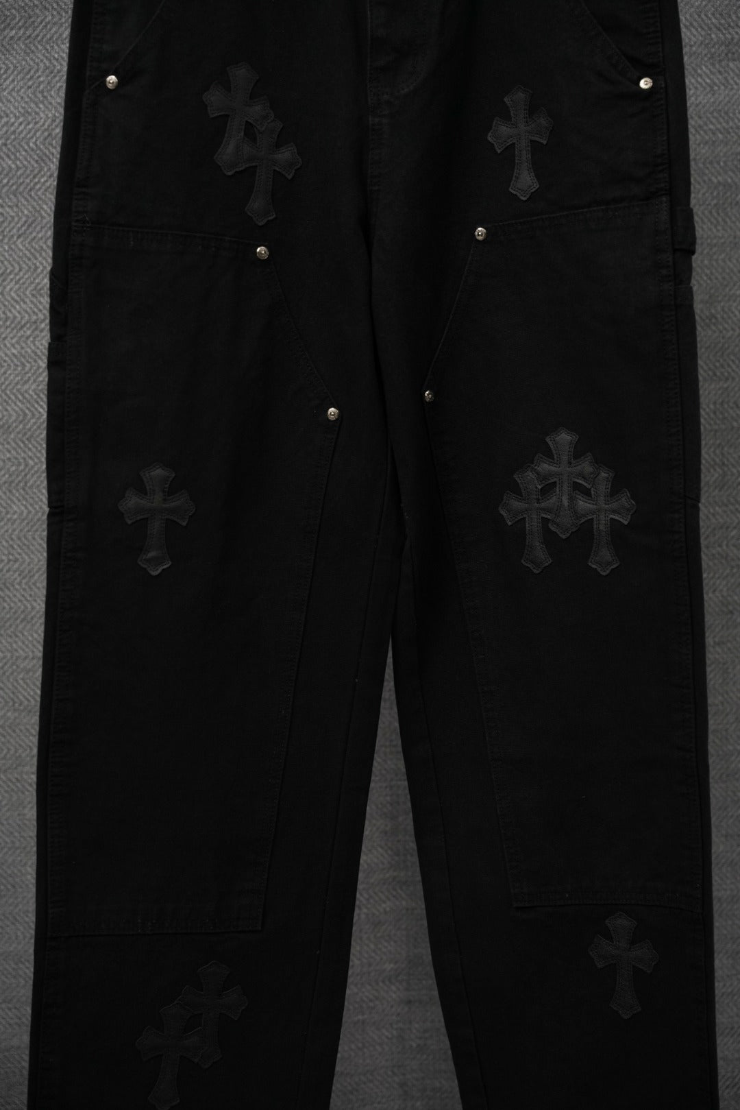 Black cargo pants with silver snap buttons and scattered cross patches on front