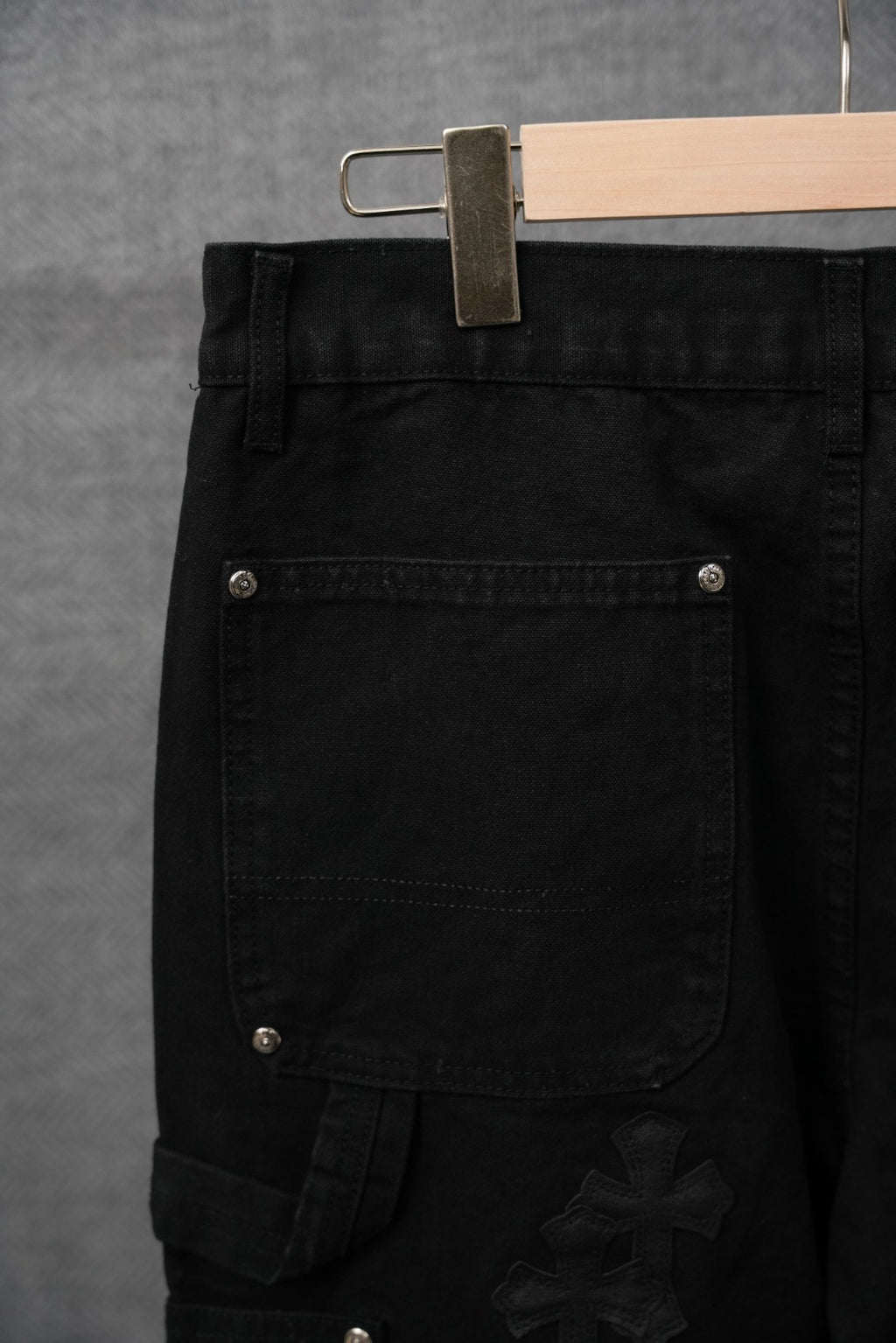 Black pants detail with flap pocket, metal snap, and cross applique