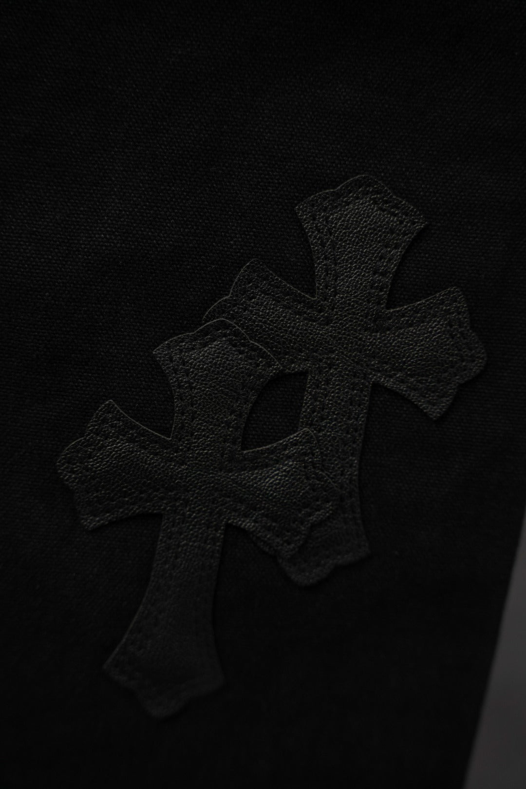 Black pants fabric close-up with raised cross applique