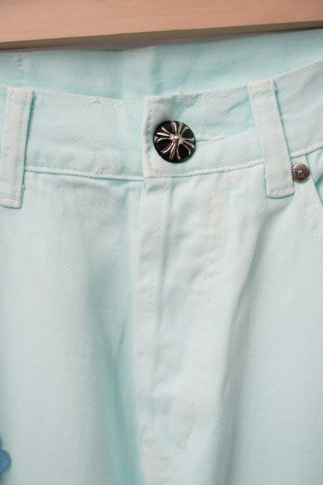 Light blue denim pants waistband with a black snap button and belt loops.