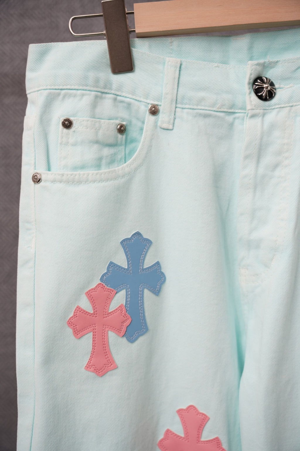 Light blue denim pants with pink and blue cross patches on the front leg.