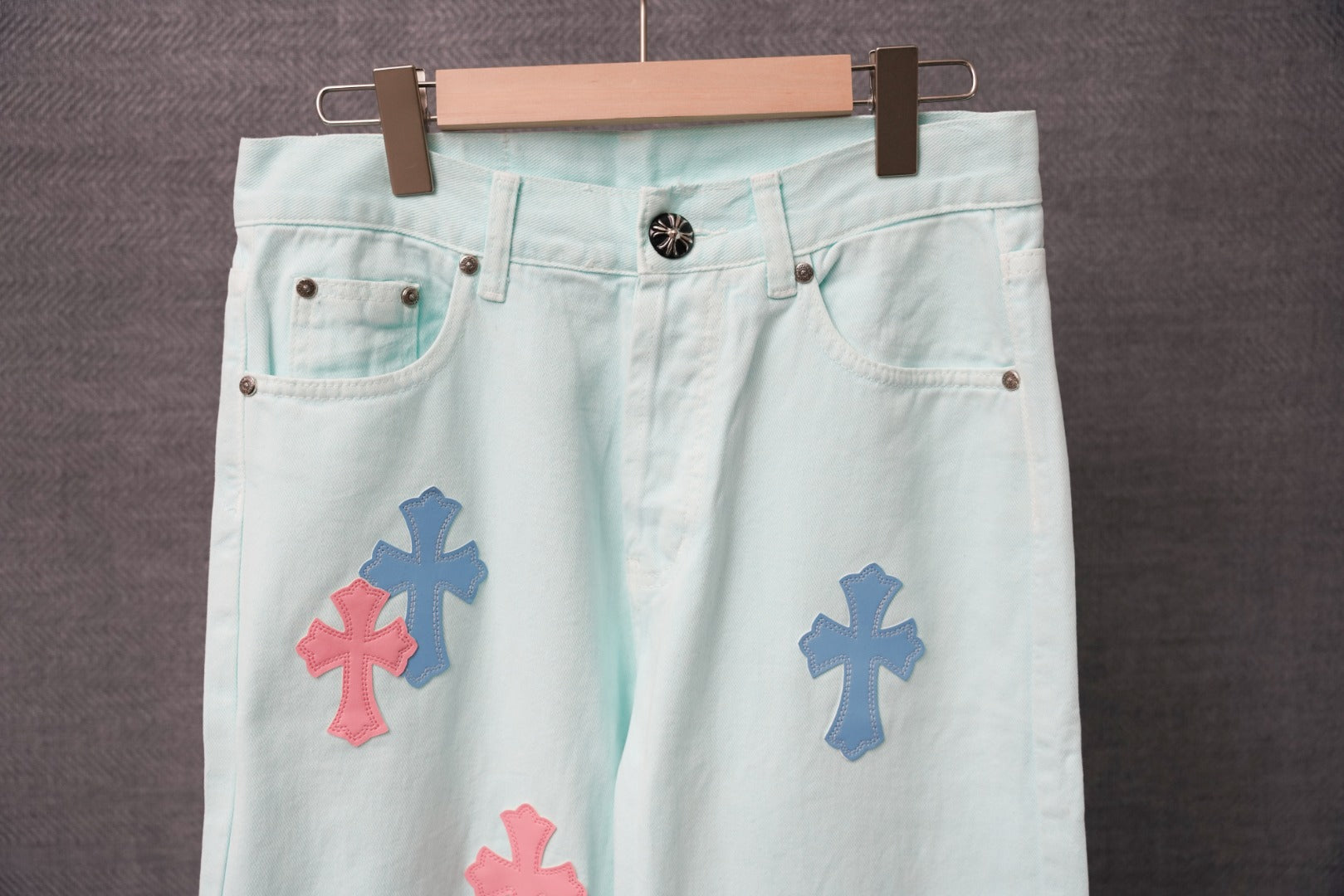 Light blue denim pants with multiple colorful cross patches and a black waistband button.