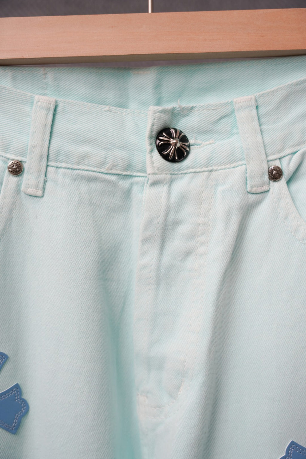 Light blue denim pants waistband with a black snap button and belt loops.