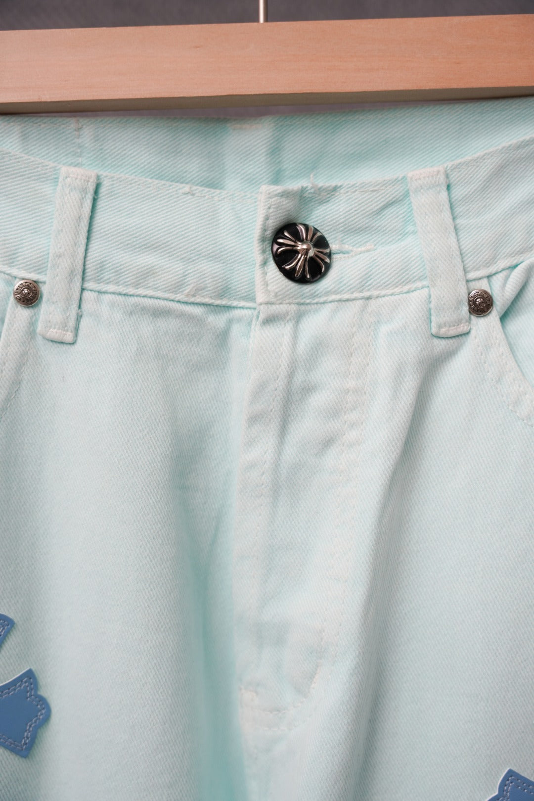Light blue denim pants waistband with a black snap button and belt loops.