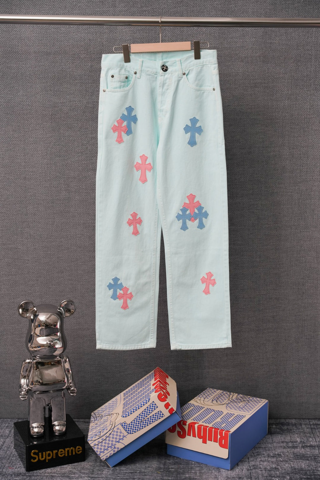 Light blue denim pants with colorful cross patches, button and zipper front.