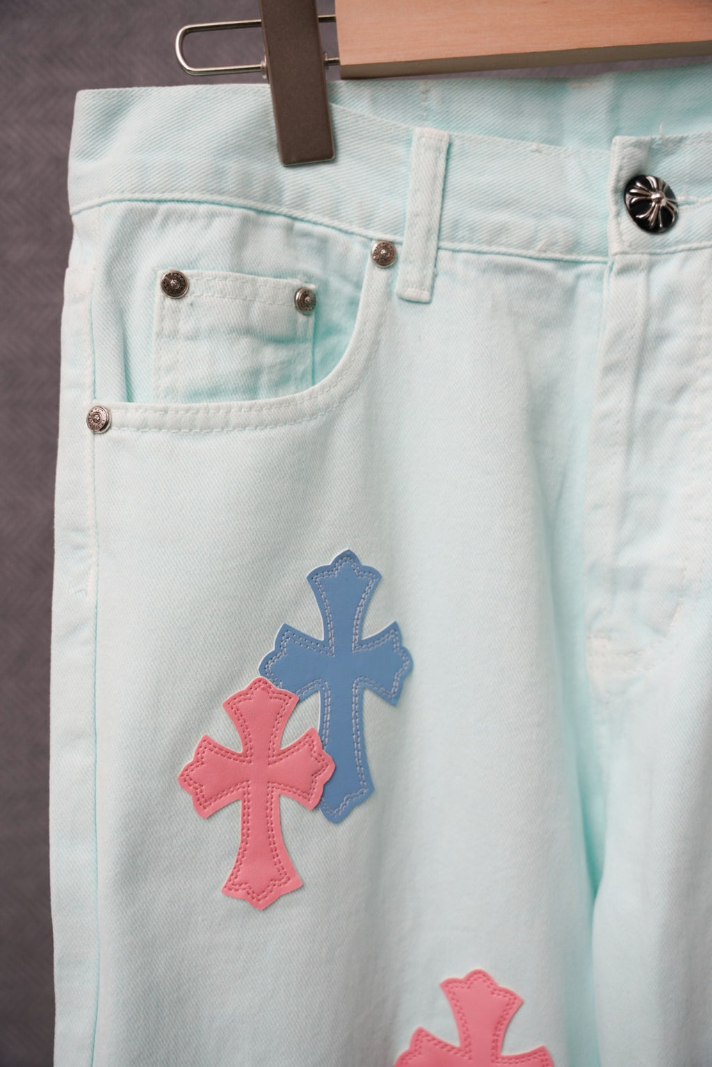 Light blue denim pants close-up of cross applique near front pockets