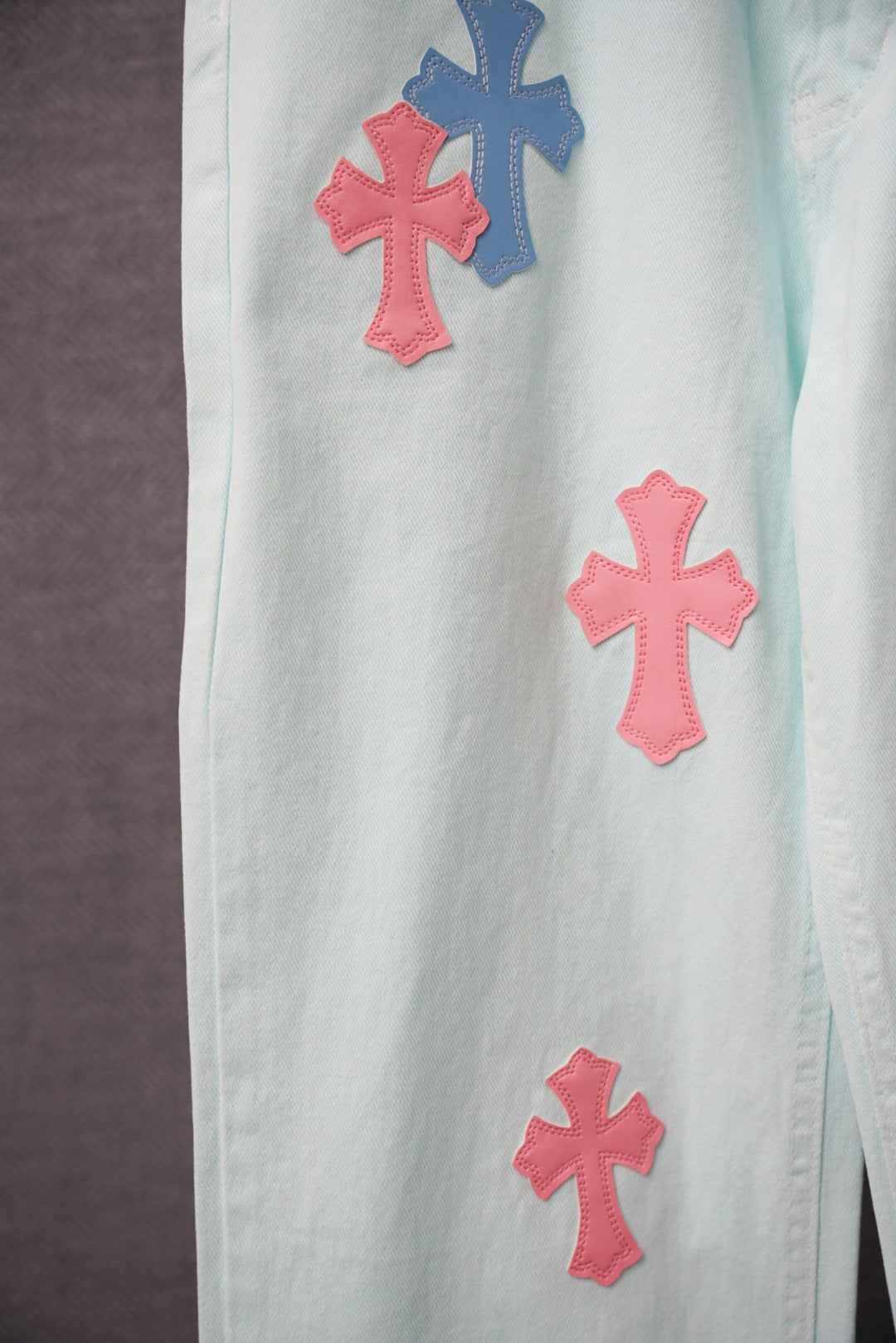Light blue denim pants leg close-up with pink and blue cross patches