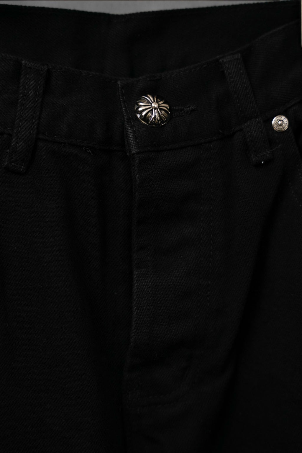 Black pants waistband with button closure and decorative silver shell emblem
