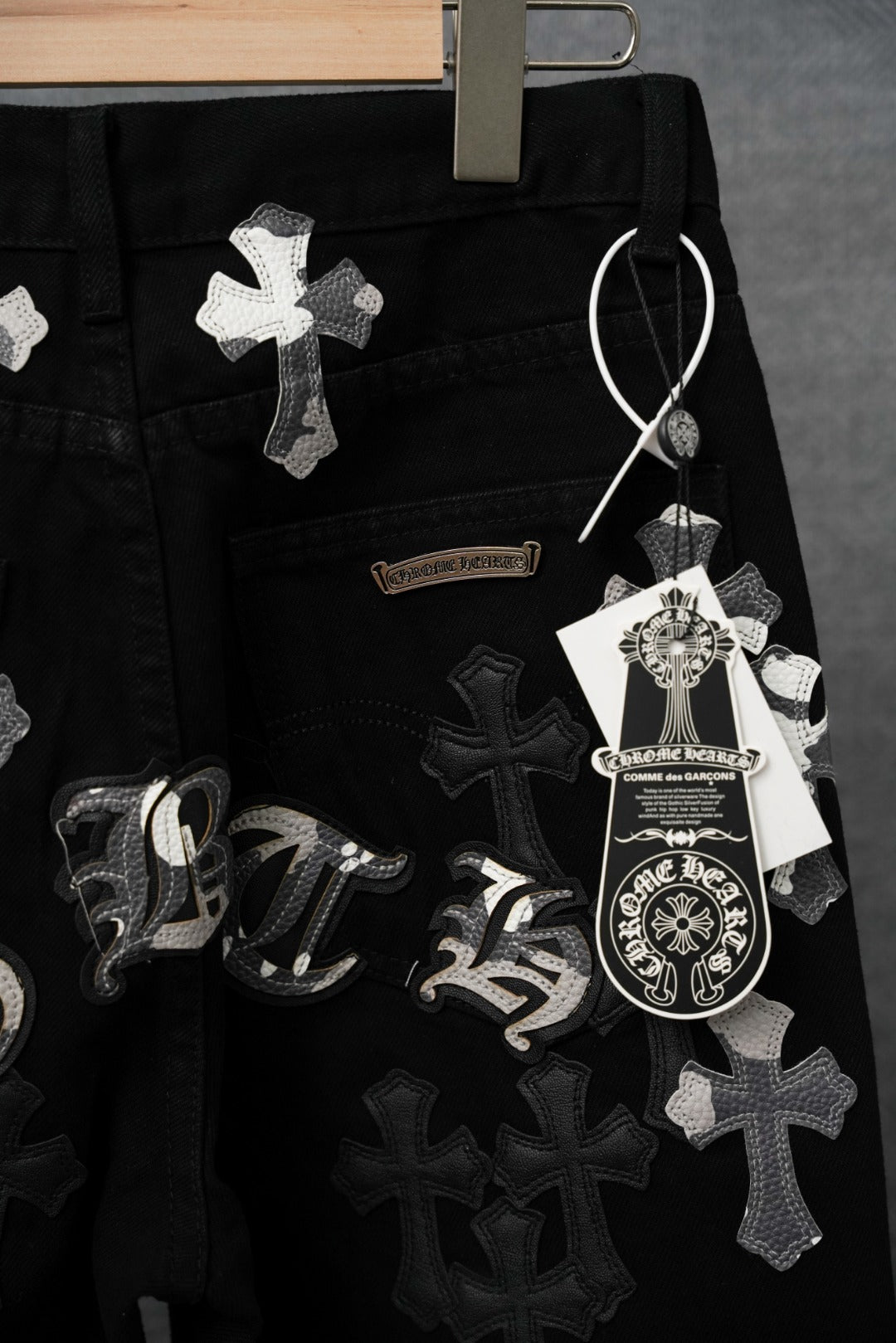 Black pants with cross patches, cursive lettering detail, and hanging tag