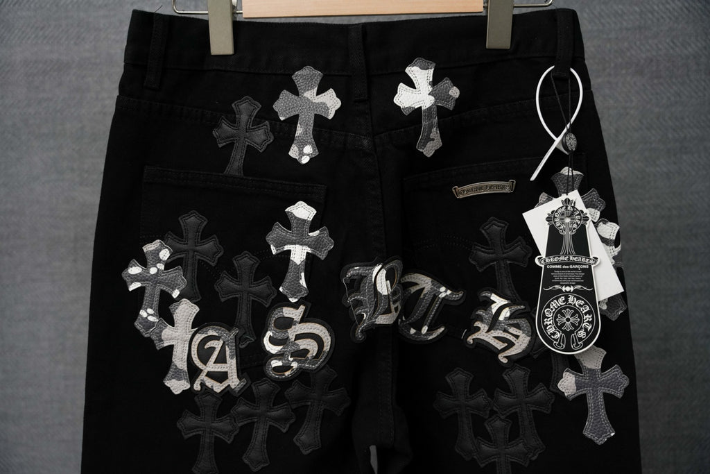 Black pants with cross patches, ornate emblem, and hanging tag on the waist