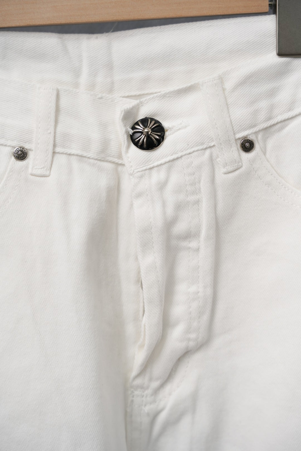 Close-up of white pants waistband with button, fly placket, and pocket details