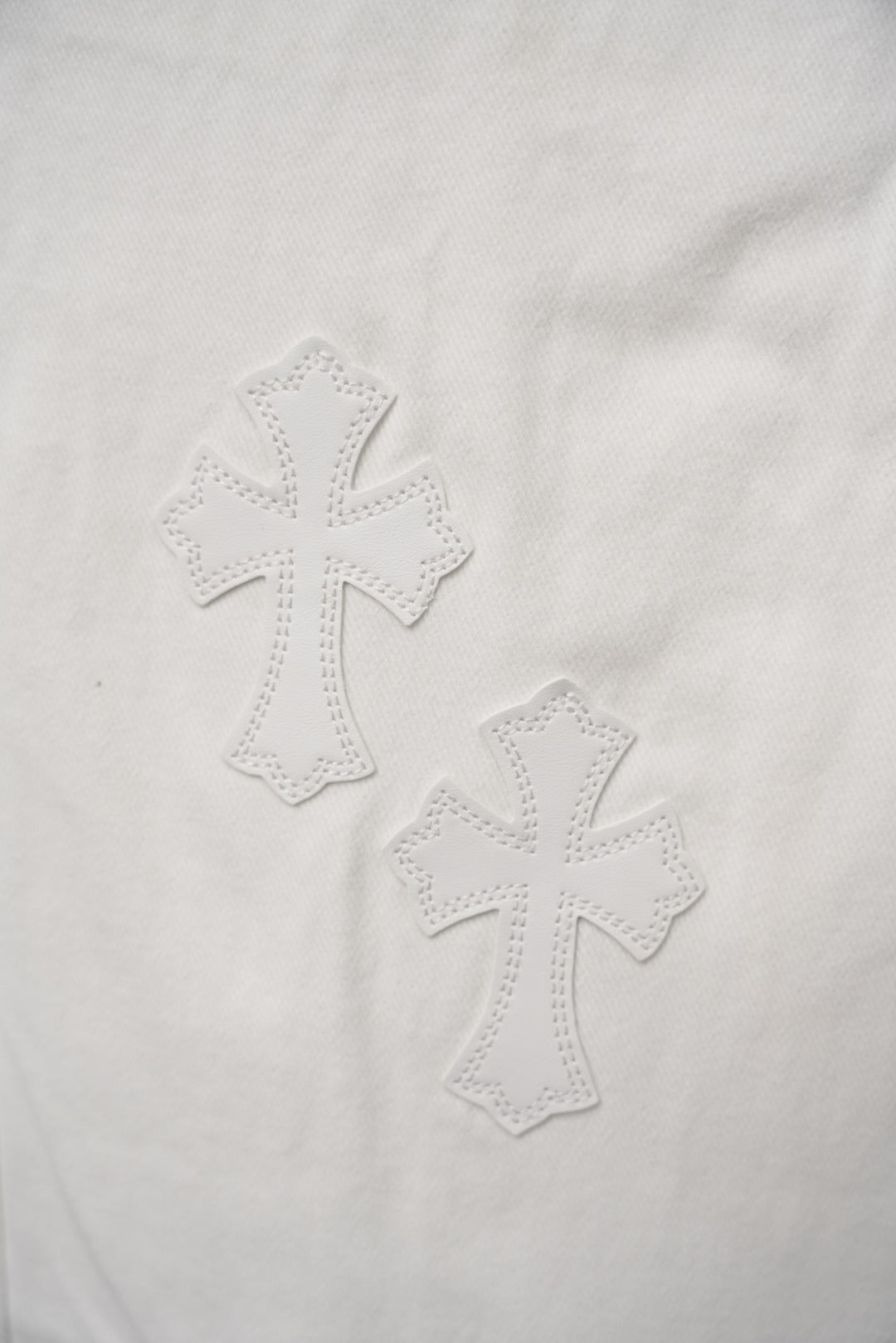 Close-up of stitched cross motifs on white pants fabric