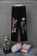 Black cargo pants with colorful embroidered graphic patches on legs, front view